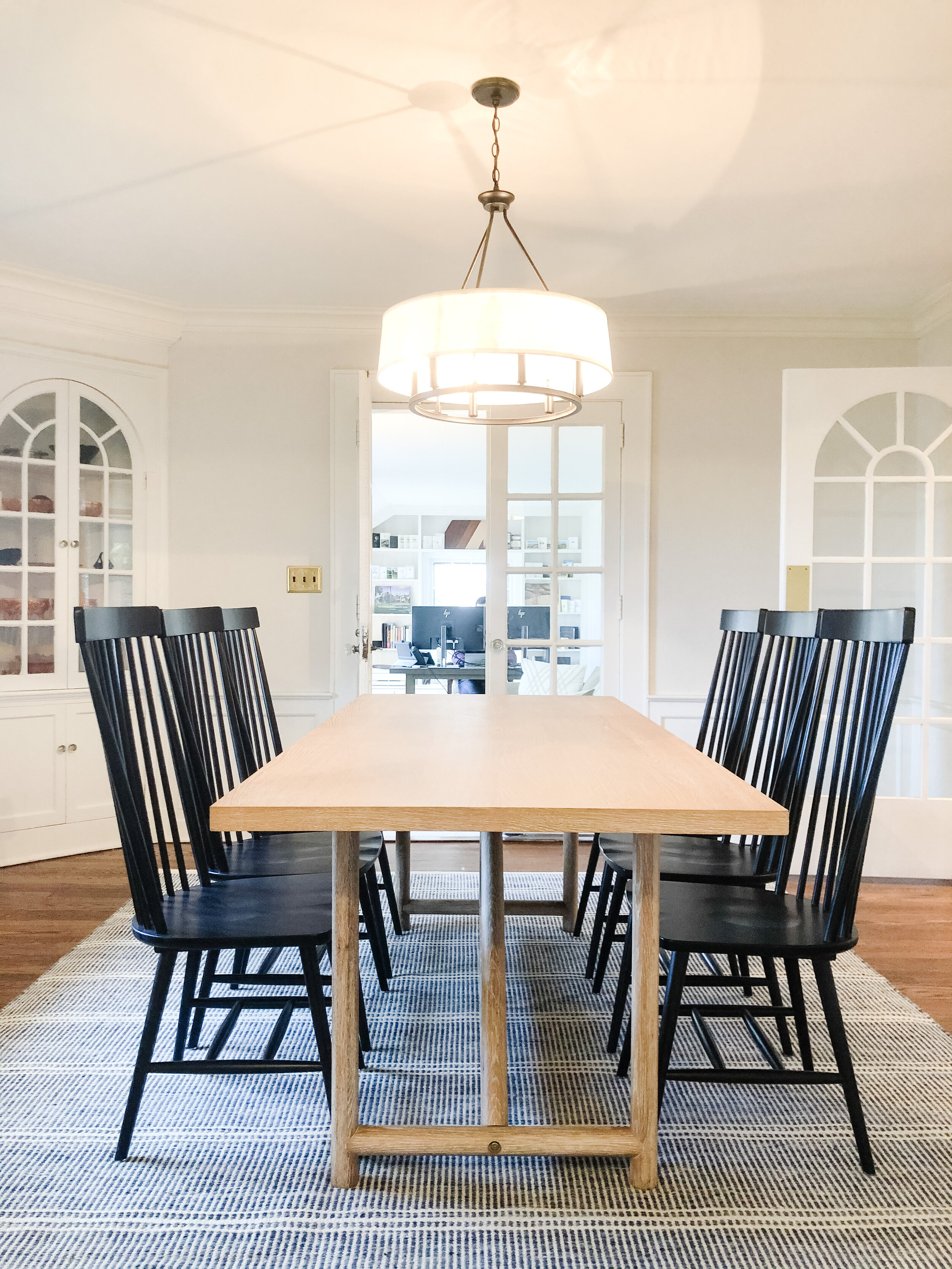 Dining room with a white oak table, black spindle chairs and a drum pendant set between arched windows in a Summit, New Jersey home by Ellie Mroz Design.