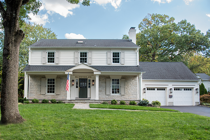 The same Westfield, New Jersey home after renovation, refaced in stone with a columned portico, new shutters and a rebuilt garage elevation across the lawn.