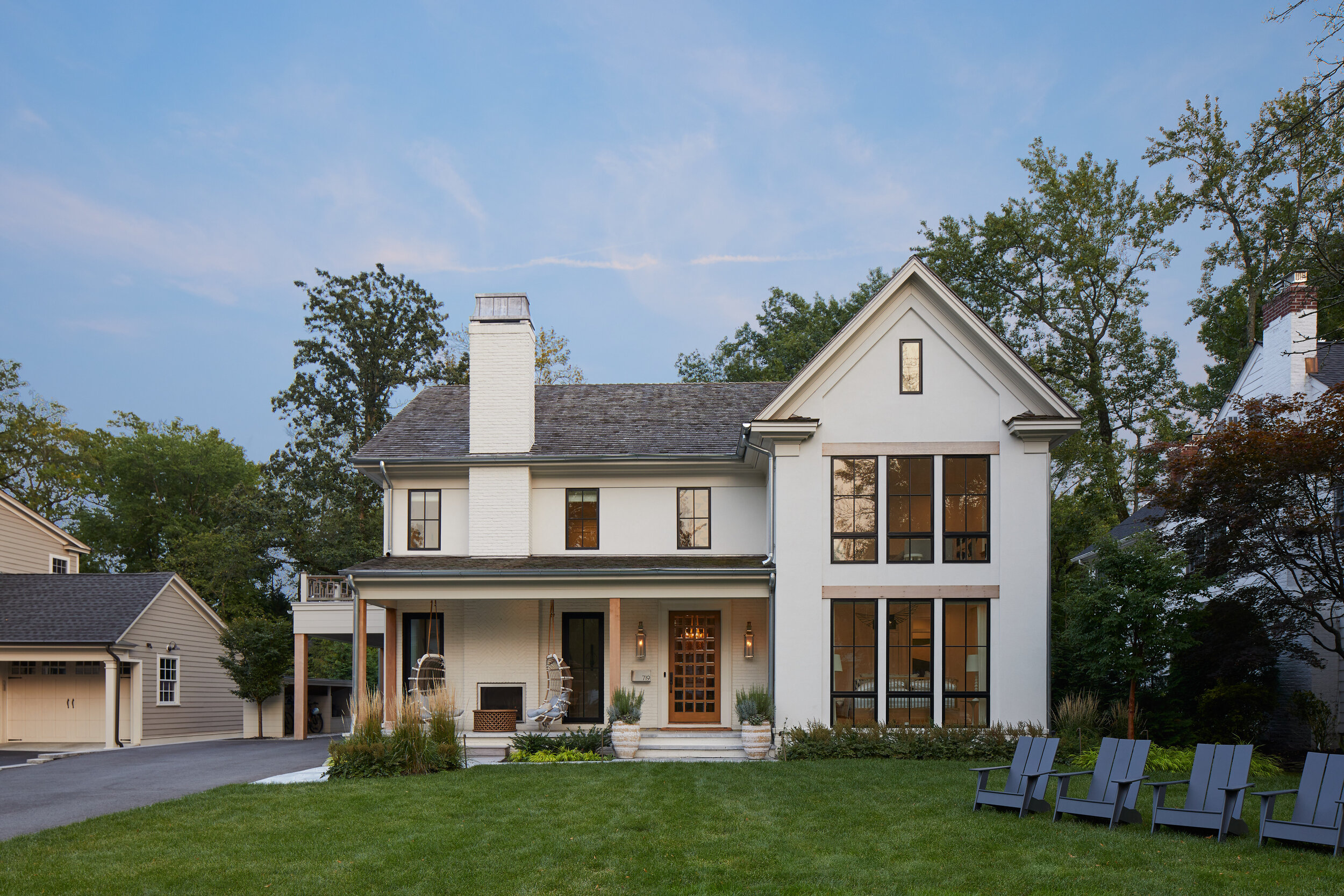 Modern farmhouse exterior at dusk with a lit covered porch, black-framed windows and brick detailing in a Westfield, NJ new-construction home by Ellie Mroz Design.