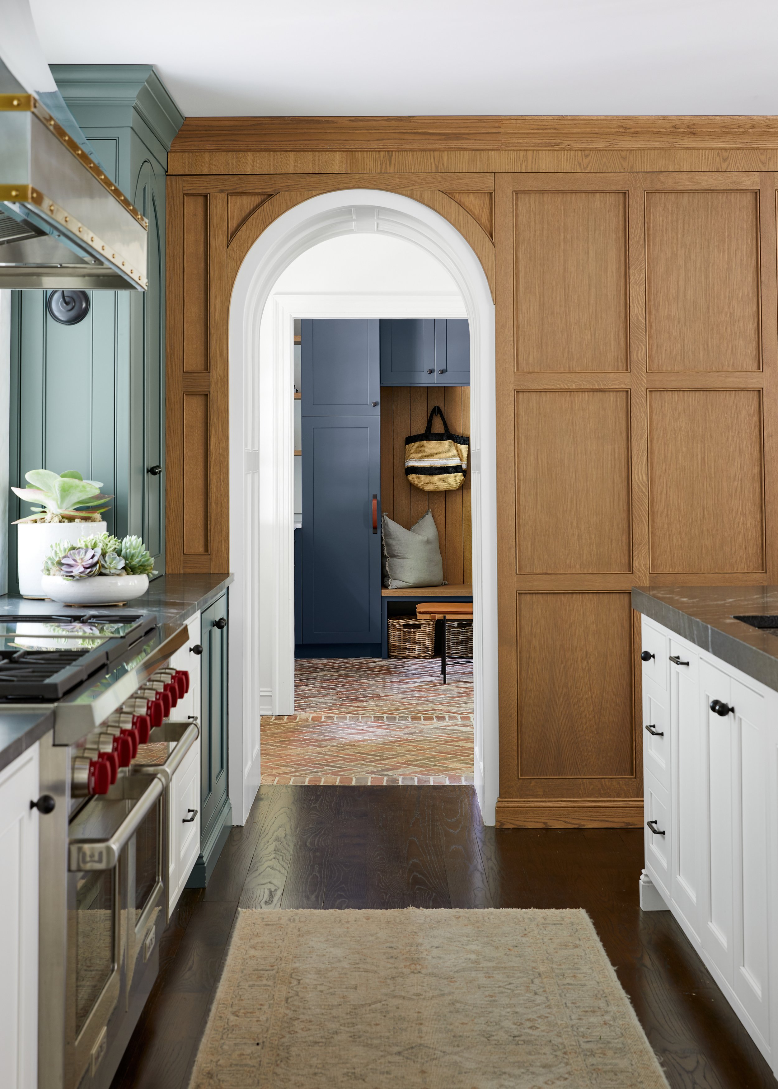 Kitchen with sage green cabinetry, a black range wall and an arched white oak doorway through to the mudroom in a 1929 Westfield, New Jersey renovation by Ellie Mroz Design.