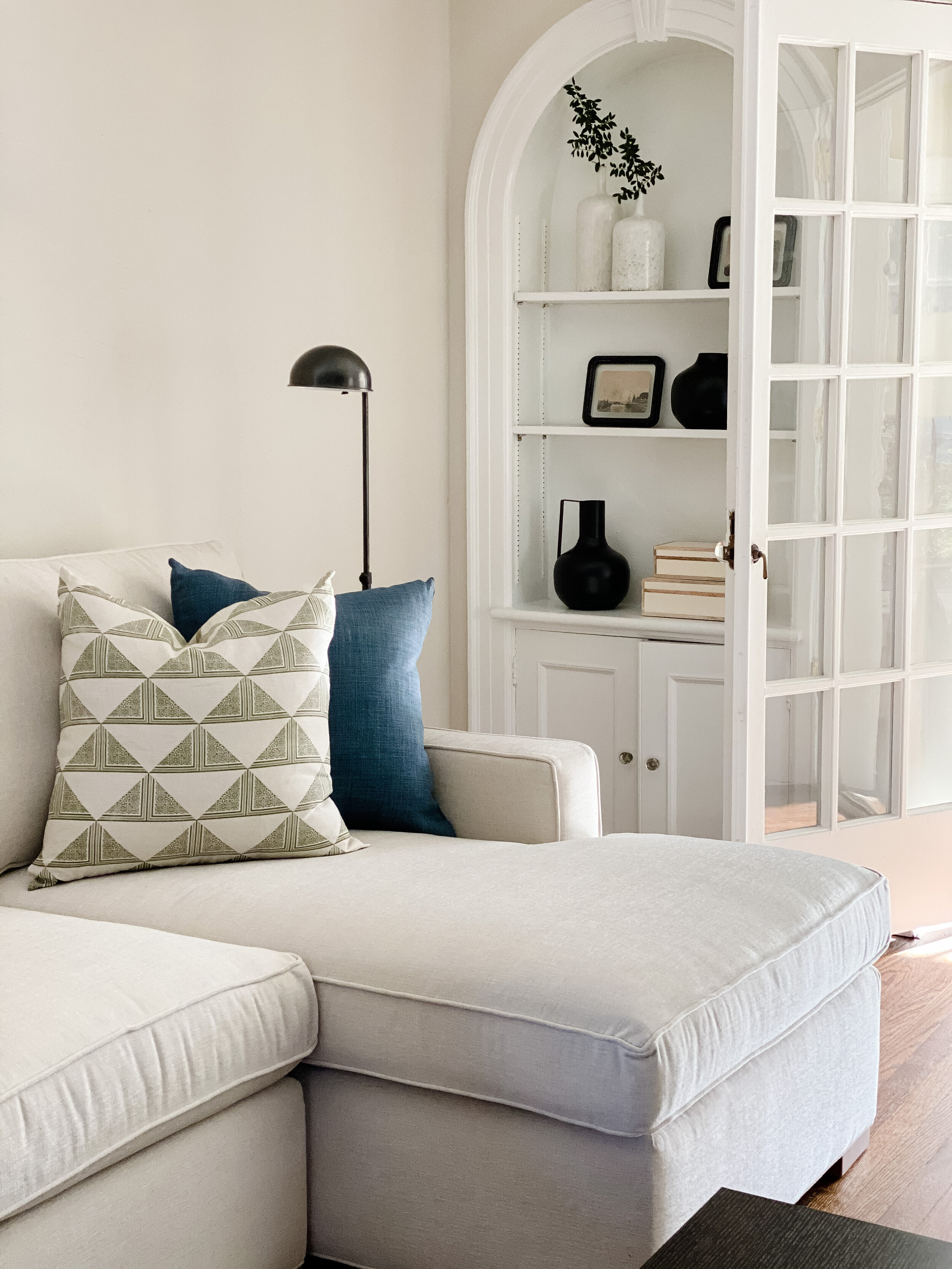 Cream sectional with block-print pillows beside an arched built-in nook with open shelving in a Summit, New Jersey home by Ellie Mroz Design.